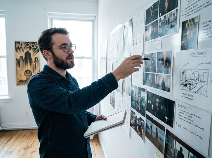 Jeune étudiant présentant un story-board de projet cinéma d'animation 3D devant un mur de références visuelles